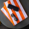 Black JBL Flip 5 Bluetooth speaker lying on a towel next to a pair of shades